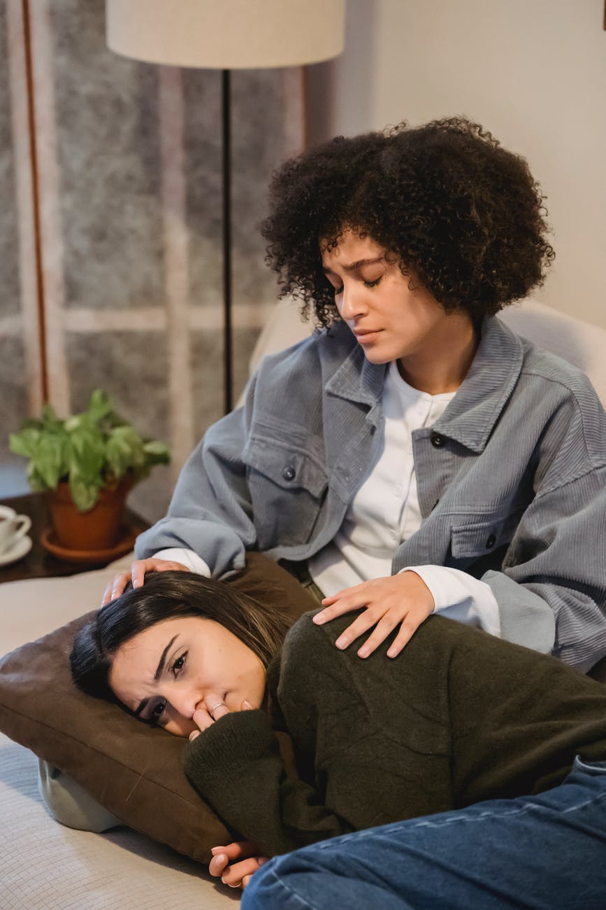 young melancholic woman lying on couch near black female friend